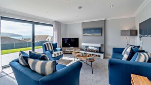 Een moderne woonkamer met een grote televisie, comfortabele zitplaatsen en uitzicht op zee.