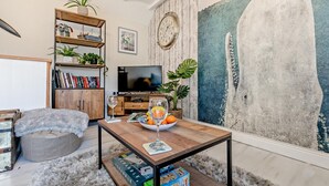 A cozy living room with a wooden coffee table, a bookshelf, a flat-screen TV, and a large abstract painting on the wall. - 1 Bed in Mevagissey (oc-h27460) (Mevagissey)