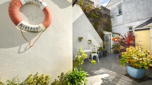 A small courtyard with a white wall, a lifebuoy, and a few potted plants. - 1 Bed in Mevagissey (oc-h27460) (Mevagissey)