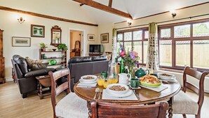 A dining area with a wooden table set for breakfast, a leather sofa, and a TV in the background.