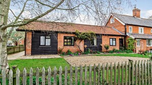 A traditional brick house with a black front door, a small garden, and a wooden fence.