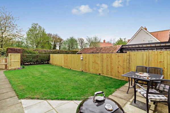 A backyard with a wooden fence, a lawn, and a patio with a table and chairs.