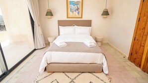 Quarto de hotel com cama, mesas de cabeceira, um quadro na parede e vista pela janela.