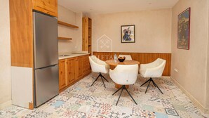 Cozinha compacta com armários de madeira, geladeira de aço inoxidável, mesa de jantar com quatro cadeiras e piso estampado.