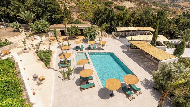 Área de piscina com espreguiçadeiras e guarda-sóis, rodeada por vegetação e colinas.