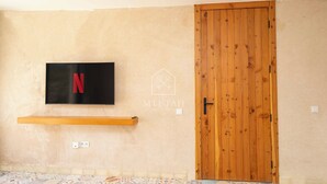 Um quarto com porta de madeira, televisão montada exibindo o logotipo da Netflix, e piso estampado.