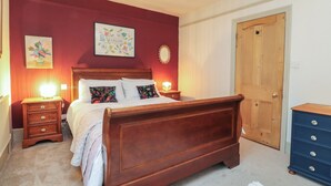 Une chambre à coucher avec un lit en bois, deux tables de chevet, une commode, une porte et des éléments de décoration murale.