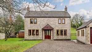 Une maison en pierre avec une entrée centrale, de nombreuses fenêtres et une allée gravillonnée.