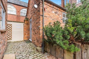 A narrow cobblestone alleyway leading to a brick building with a small door and a clock on the wall. - 1 Bed in Whitby (oc-d27454) (Whitby)
