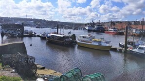 Un port amb diverses embarcacions amarrades, un pont i edificis al fons.