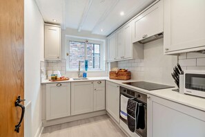 A compact kitchen with white cabinets, a built-in oven, a microwave, and a window with a view of a brick wall. - 1 Bed in Whitby (oc-d27454) (Whitby)