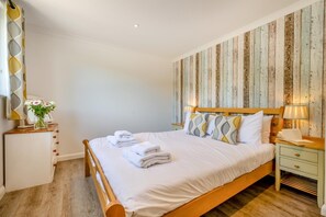 A neatly made bed with white linens and towels, a wooden headboard, and a bedside table with a lamp and a book. - 4 Bed in St. Levan (oc-b27515) (Saint Levan)