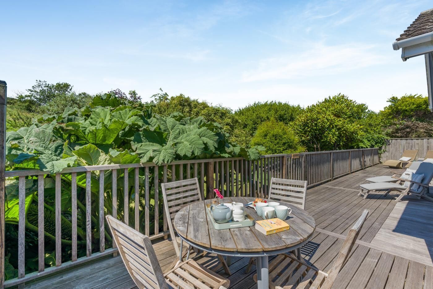 A wooden deck with a round table and chairs, surrounded by a wooden fence and lush greenery.