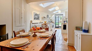 Un coin repas avec une table en bois dressée pour quatre personnes, une cuisine en arrière-plan et une lucarne au-dessus.