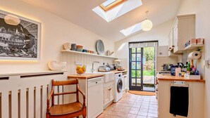 Une cuisine moderne avec une lucarne, un coin repas doté d’une chaise en bois et une vue sur le jardin par la porte.