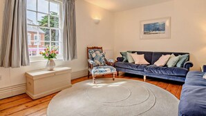 Un salon avec un canapé bleu, un fauteuil à motifs, un radiateur blanc et une fenêtre avec des rideaux.