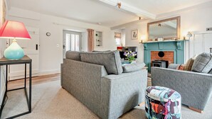 Un salon comprenant un canapé, un fauteuil et un pouf, une cheminée et un téléviseur.