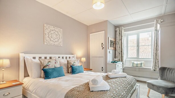 Une chambre bien rangée, avec un lit, des tables de chevet, une chaise et une fenêtre avec des rideaux.