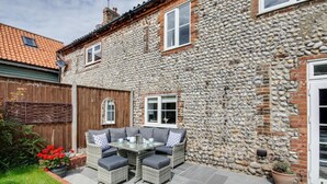 Une maison en pierre avec un patio, du mobilier d’extérieur et une clôture en bois.