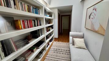 Una habitación con una estantería blanca llena de libros, una alfombra con diseño y un sofá gris con un cojín.