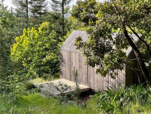 A wooden cabin with a sloped roof, surrounded by dense greenery and trees.