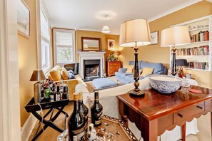 Ein gemütliches Wohnzimmer mit Kamin, Bücherregal und einem Essplatz mit Flaschen.