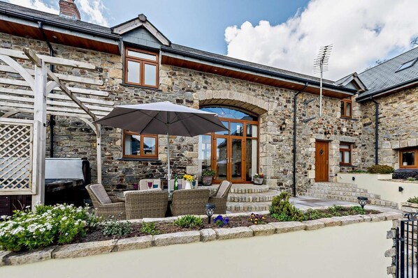 A stone building with a patio area featuring wicker furniture, a table, and an umbrella. - 3 Bed in Okehampton (oc-h27530) (South Tawton)