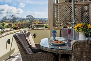 A wicker dining set with a plate of food and drinks on a balcony with a view of trees and mountains. - 3 Bed in Okehampton (oc-h27530) (South Tawton)