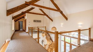 A spacious hallway with exposed wooden beams, a glass railing, and a view of the outdoors. - 3 Bed in Okehampton (oc-h27530) (South Tawton)
