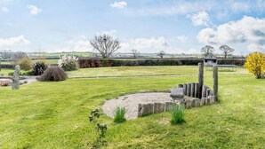 A grassy outdoor area with a stone structure, possibly a gazebo, surrounded by a gravel path and various plants. - 3 Bed in Okehampton (oc-h27530) (South Tawton)