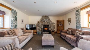 A cozy living room with a stone fireplace, two sofas, a television, and a bookshelf. - 3 Bed in Okehampton (oc-h27530) (South Tawton)