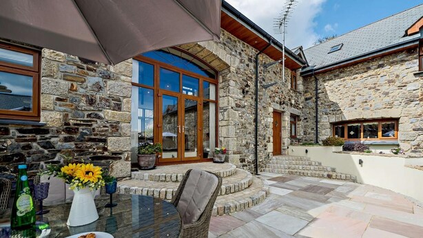 A stone building with a glass door entrance, outdoor seating area, and a table with food and drinks. - 3 Bed in Okehampton (oc-h27530) (South Tawton)
