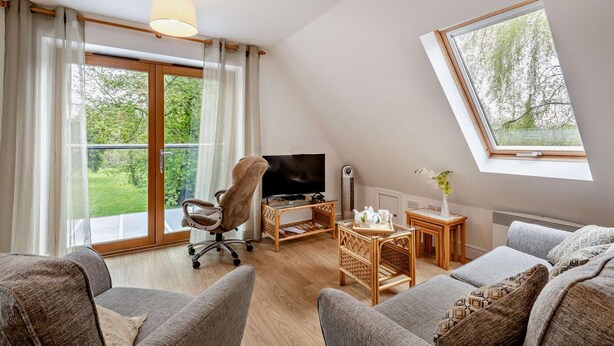 A cozy living room with a TV, comfortable seating, a small table, and a window with a view of greenery. - 2 Bed in Eccles (oc-l27507) (Eccles)