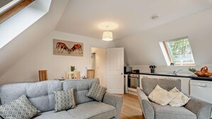 A modern loft apartment with a grey sofa and armchair, a dining area, a kitchen with a window, and a ceiling light. - 2 Bed in Eccles (oc-l27507) (Eccles)