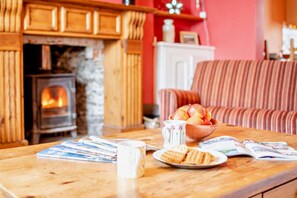 Ein gemütliches Wohnzimmer mit Kamin, einem gestreiften Sofa, einem Tisch mit Zeitschriften, einer Obstschale und einer Tasse.