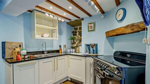 A kitchen with white cabinets, a black stove, and a stone accent wall. - 3 Bed in Hawes (oc-hhmy23) (Hawes)