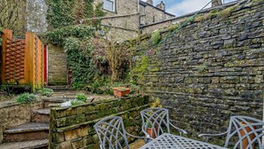 A stone wall with a metal table and chairs in a garden area, surrounded by greenery and a wooden fence. - 3 Bed in Hawes (oc-hhmy23) (Hawes)