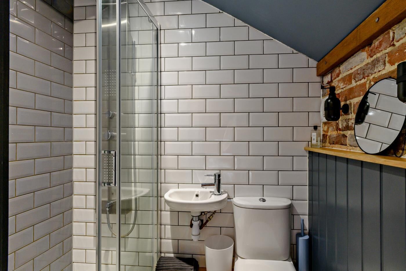 Ein modernes Badezimmer mit weißen Fliesen im U-Bahn-Stil, einer Duschkabine aus Glas, einem Waschbecken und einer Toilette.
