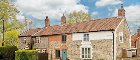 A traditional stone house with a tiled roof, a green door, and a sign indicating 'BACKLANE'.