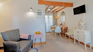 A cozy living room with a grey sofa, a small pink side table with fruit, a white dresser, and a TV mounted on the wall. - 2 Bed in Cromer (oc-s1149) (Cromer)