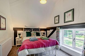 Un dormitorio con cama, mesita de noche, lámpara y ventana con cortinas.