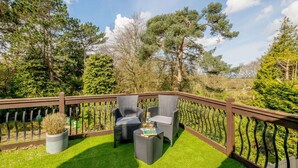 Une terrasse dotée de meubles en osier et d’une petite table, entourée d’une balustrade en bois et d’une végétation luxuriante.