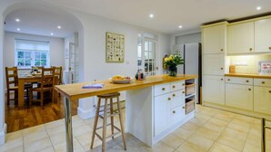 Une cuisine moderne avec des meubles blancs, un îlot central en bois et un coin repas comprenant une table et des chaises en bois.
