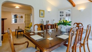 Une salle à manger avec une table en bois dressée pour six personnes, entourée de chaises en bois. Un vase rempli de fleurs est posé sur la table, et on aperçoit une cheminée au fond de la pièce.