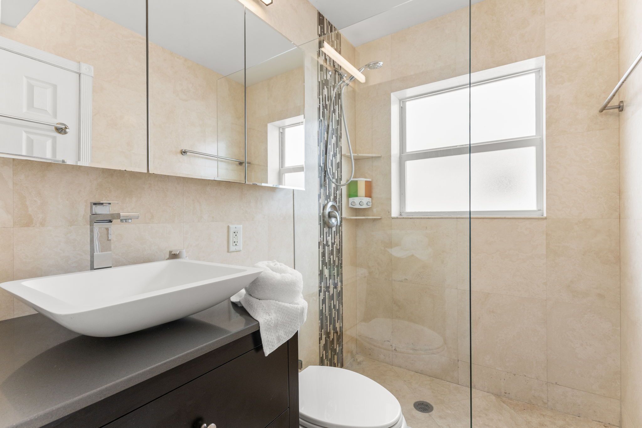 A modern bathroom with a large vessel sink, a toilet, a shower with a glass door, and a mirror above the sink.