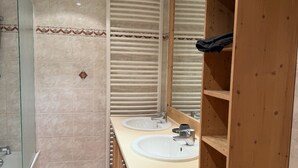 A bathroom with two sinks, a glass shower enclosure, and wooden shelving.