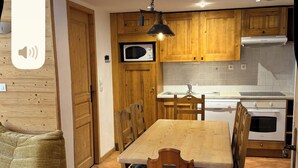 A compact kitchen with wooden cabinets, a dining table with chairs, and a tiled floor.