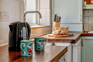 A kitchen with a kettle, two mugs, a loaf of bread, and a knife block.