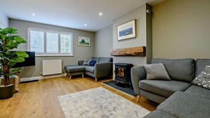 A cozy living room with a fireplace, grey sofas, a large plant, and a TV. - 3 Bed in Ruswarp (oc-wa264) (Ruswarp)