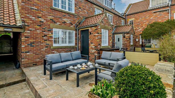 A brick house with a patio area featuring a sofa set and a table with teacups. - 3 Bed in Ruswarp (oc-wa264) (Ruswarp)